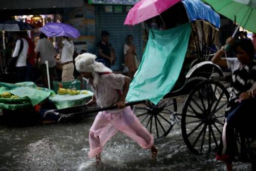 Un uomo con il risciò per le strade allagate in India